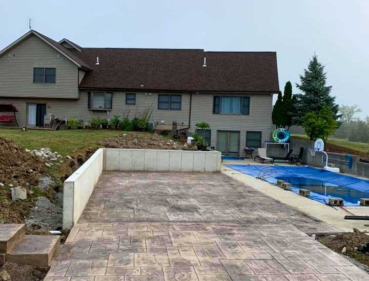 new retaining wall, stamped patio and steps beside the swimming pool at the back of a house
