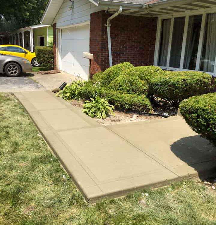 colored concrete sidewalk connecting the garage of a house with landscaped lawn